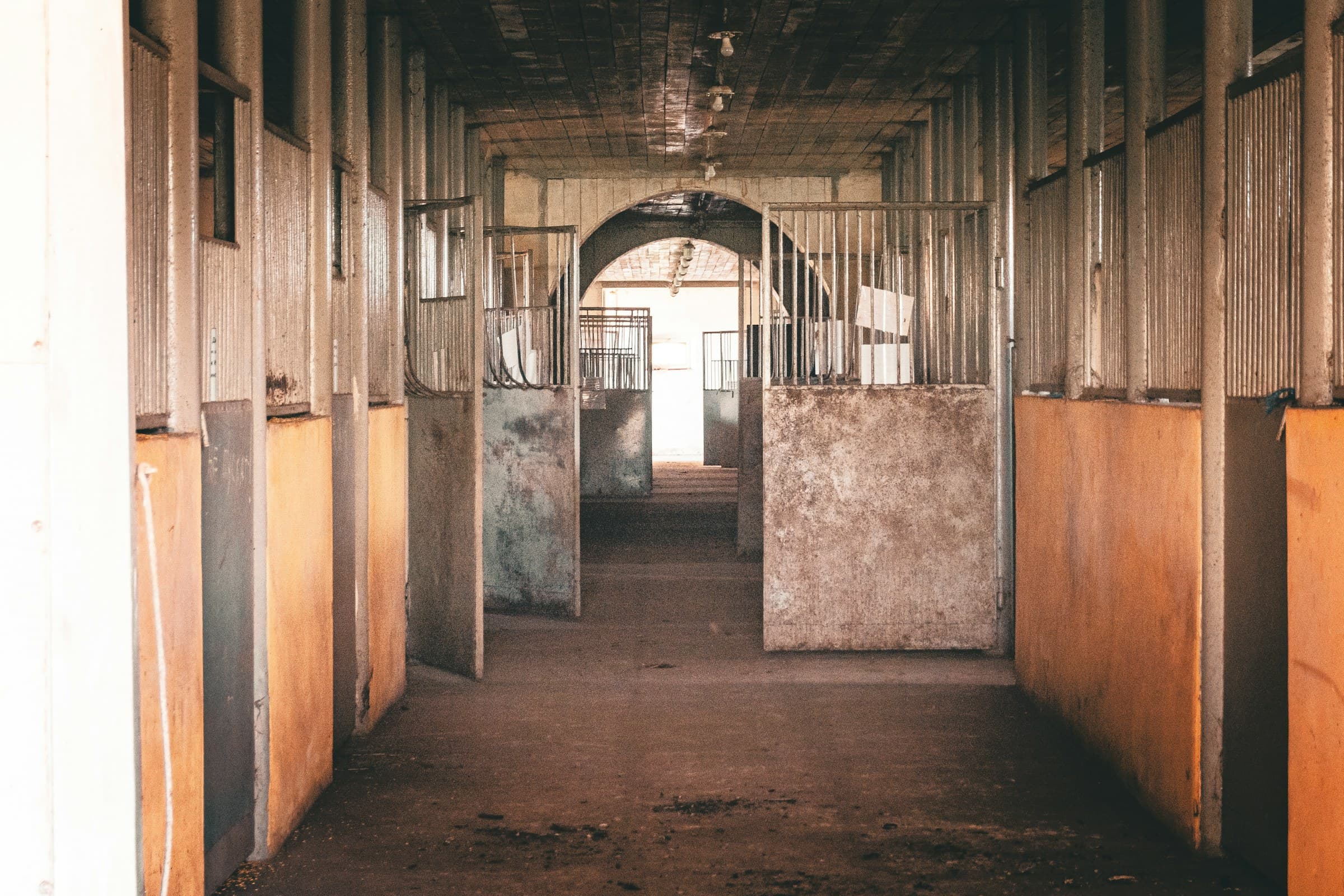 The dim central aisle of a wooden horse barn, stall doors running down both sides