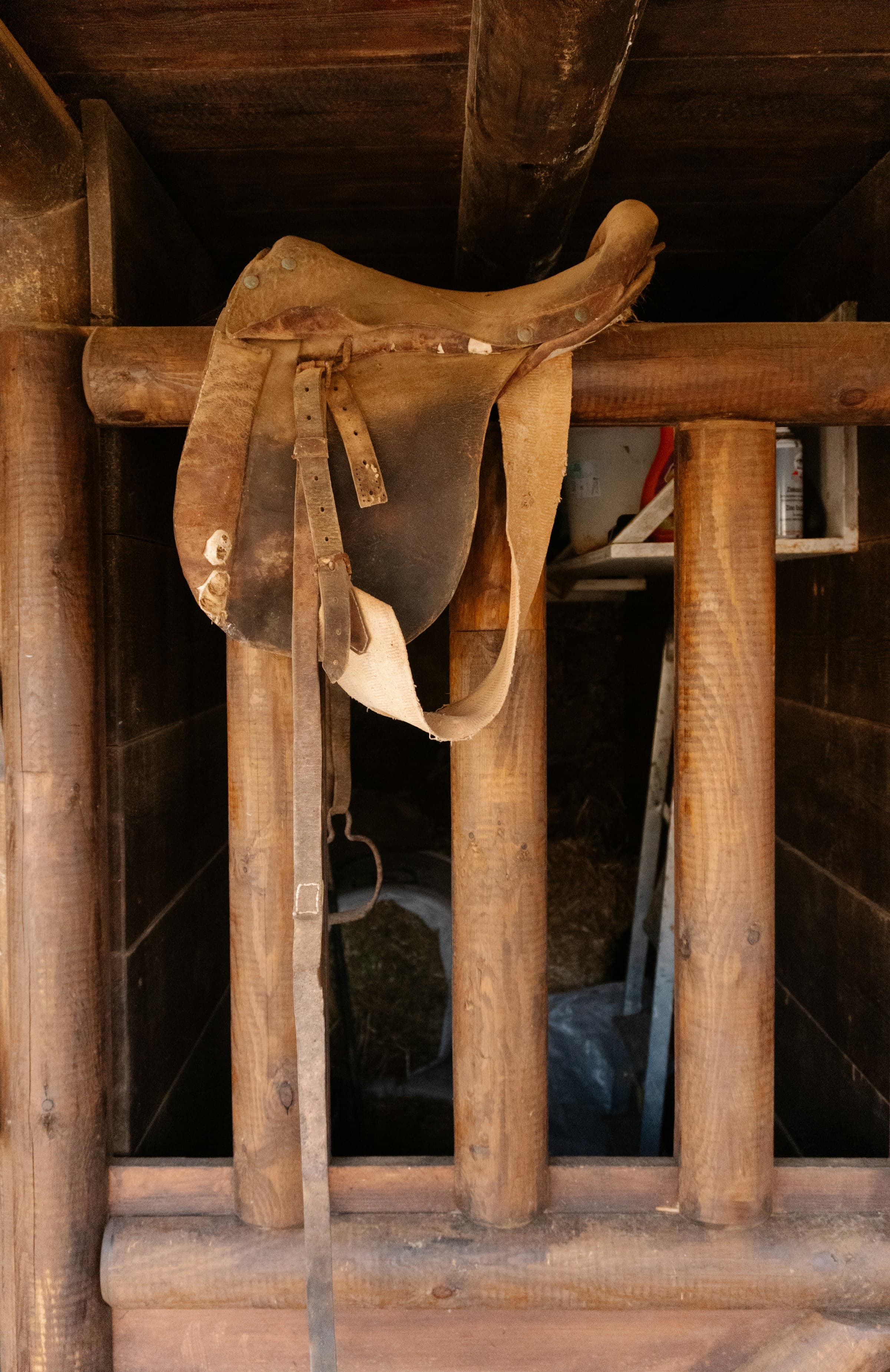 A worked saddle and stirrup hanging on a wooden rack in a tack room